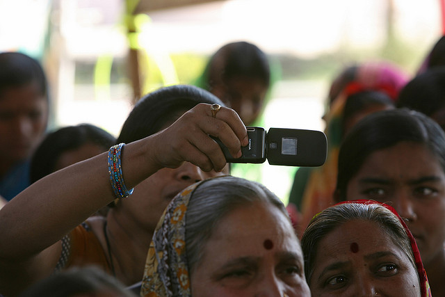 Woman takes photo with cellphone at a community meeting credits World Bank photo collection via Flickr ((CC BY-NC-ND 2.0) )